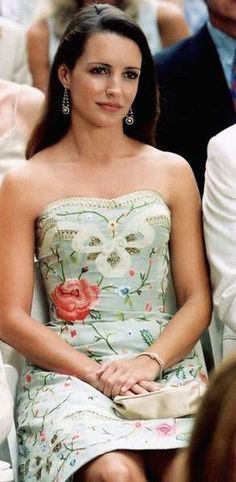 a woman in a floral dress sitting on a chair at a formal event with other people