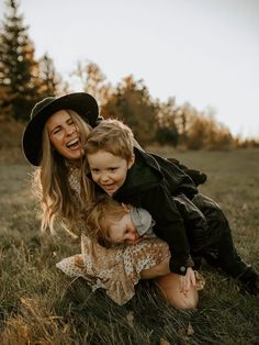 a mother and her two children are playing in the grass with one child wearing a cowboy hat