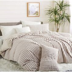 a bed with white sheets and pillows in a room next to a potted plant