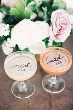 two wine glasses with names on them and flowers in the background