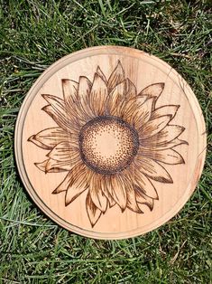 a wooden plaque with a sunflower on it sitting in the grass next to some green grass