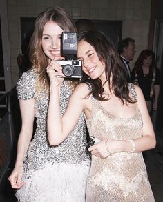 two women standing next to each other holding up a camera