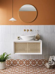 a white sink sitting under a round mirror next to a potted plant on top of a counter