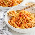 two white bowls filled with pasta on top of a table next to a wooden spoon