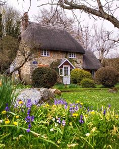 a house with a thatched roof surrounded by flowers and trees in front of it