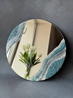 a round mirror sitting on top of a wall next to a vase with flowers in it