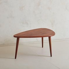 an oval wooden table sitting on top of a white floor next to a concrete wall