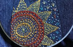 a close up of a embroidery on a piece of cloth with an orange and blue flower