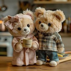 two teddy bears dressed in clothes and holding coffee mugs on a wooden table next to each other