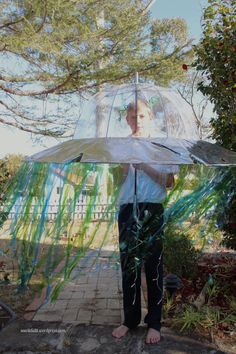 a person standing under an umbrella on a sidewalk with trees in the background and grass growing all around them