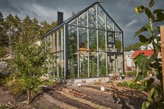 a house with glass walls and plants growing inside the front yard, on a cloudy day