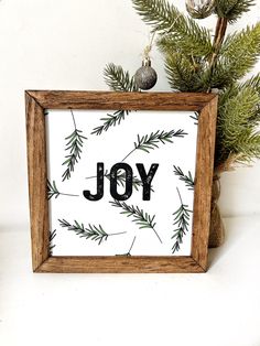 a wooden frame with the word joy painted on it next to a christmas tree branch