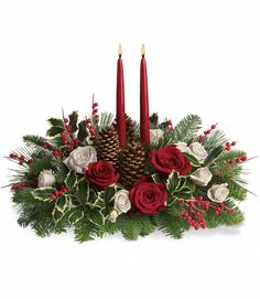 a christmas centerpiece with two candles and evergreens in the center, surrounded by red roses