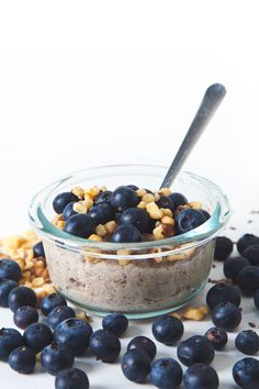 a glass bowl filled with blueberries and granola on top of a white table