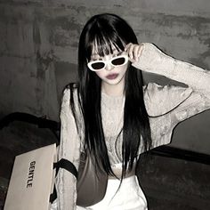 a woman with long black hair wearing sunglasses and holding a bag in front of her face