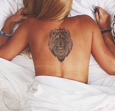 a woman laying in bed with a lion tattoo on her upper back and right arm