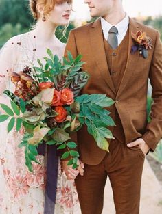 a man and woman standing next to each other with flowers in their hair, wearing brown suits