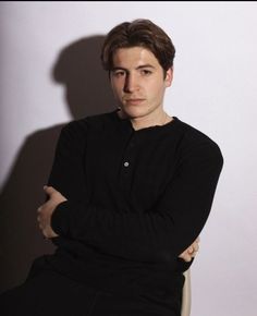 a young man sitting in a chair with his arms crossed and looking at the camera