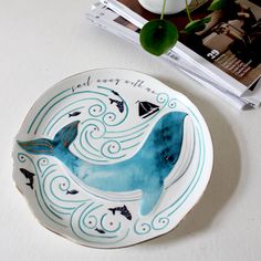 a plate with a blue whale painted on it next to a vase and magazine cover