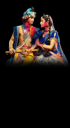 two people dressed in colorful costumes sitting next to each other on a black background,