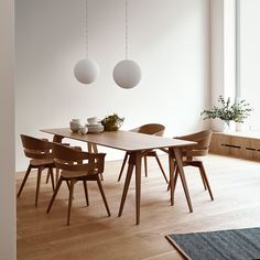 a dining room table and chairs in front of a large window with two hanging lights