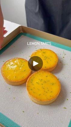 three lemon tarts sitting on top of a baking sheet in front of a person