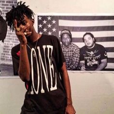 a man with dreadlocks standing in front of an american flag holding his hand to his face