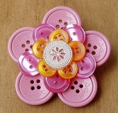 a pink flower with yellow and orange buttons on it's center sits on a wooden surface