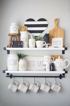 two shelves with coffee mugs and other kitchen items on top of each shelf in front of a white wall