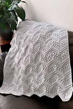 a white crocheted afghan sitting on top of a brown leather couch next to a potted plant