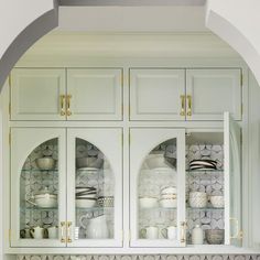 a kitchen with white cupboards and gold trim on the glass front doors is shown