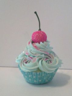 a blue cupcake with white frosting and a pink cherry on top, sitting on a table