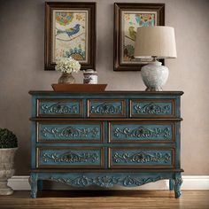 a blue dresser with two framed pictures on the wall and a lamp next to it