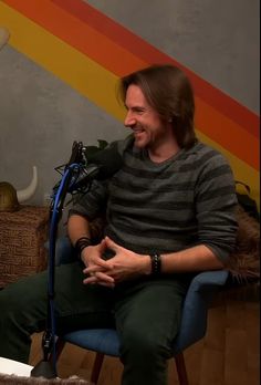 a man sitting on top of a blue chair in front of a microphone and smiling