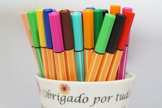 many different colored pens are in a cup with the words origado por tutas written on it