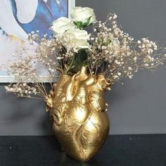 a gold vase with flowers in it sitting on a table next to a framed photograph