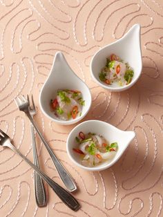 three small white bowls filled with food on top of a table next to utensils