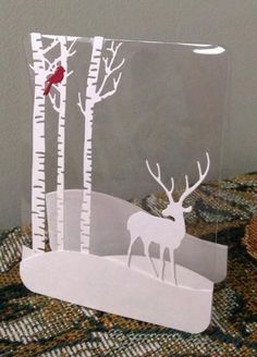 a paper cut out of a deer and trees with a bird perched on the tree