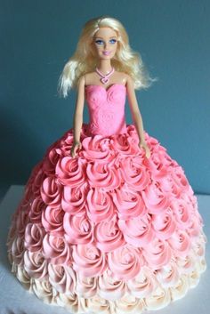 a barbie doll in a pink dress made out of roses on a tablecloth with a blue wall behind it