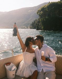 a man and woman sitting on the back of a boat kissing while holding an object in their hand