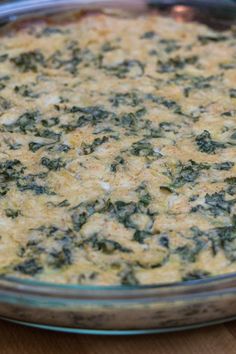 a casserole with spinach and cheese in a glass dish on a wooden table