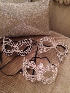 three masquerade masks sitting on top of a wooden table next to a pillow