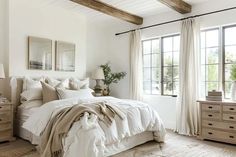 a bedroom with white bedding and wooden beams on the ceiling, two large windows