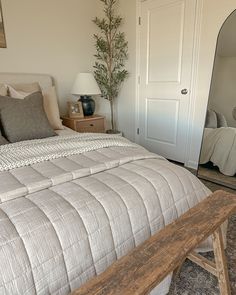 a bedroom with a bed, mirror and wooden bench in front of the door that leads to another room