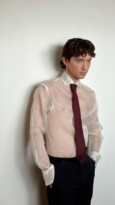 a young man in a dress shirt and tie standing against a wall with his hands on his hips