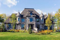 a large stone house in the middle of a grassy area with trees and bushes around it