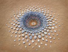 a circular design made out of rocks on the sand with water droplets in the center