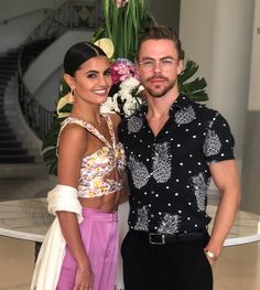 a man standing next to a woman in front of flowers