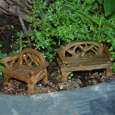 two miniature wooden benches sitting next to each other in the dirt near plants and trees