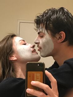 a man and woman with their faces covered in white facial maskes looking at a cell phone